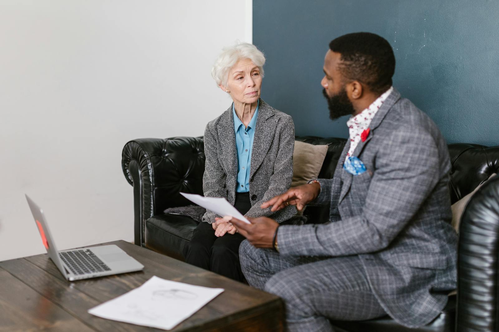 An elderly woman and a man in a professional meeting discussing documents indoors.