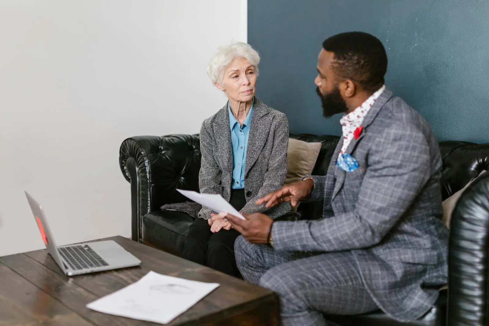 An elderly woman and a man in a professional meeting discussing documents indoors.